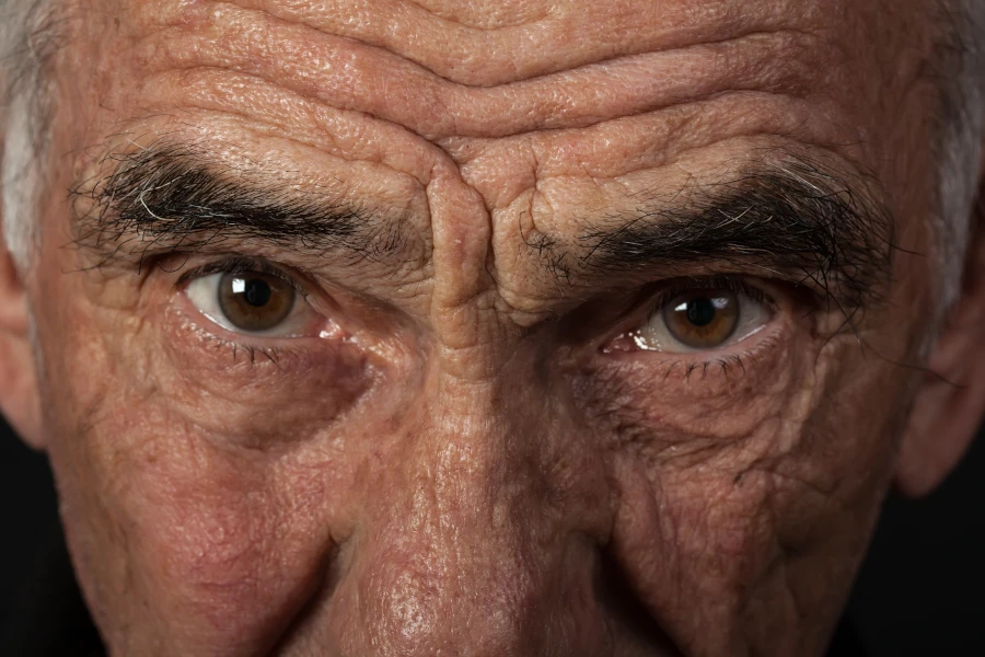 Close-up of an older man's face, focusing on his forehead, eyes, and nose, with an intense, thoughtful expression.